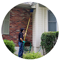 a redline pest control technician de-webbing the outside of a home